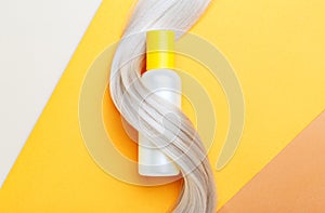 Shampoo bottle mockup strand in lock curl of blonde hair on orange color background. Yellow bottle shampoo. Flat lay copy space.