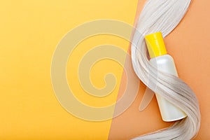 Shampoo bottle mockup strand on lock curl of blonde hair on orange color background. Yellow bottle shampoo. Flat lay copy space.