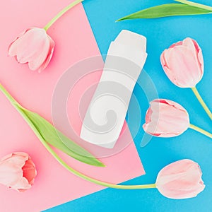 Shampoo bottle and tulips flowers on pink and blue background. Flat lay, top view. Beauty concept