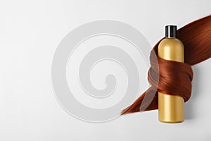 Shampoo bottle wrapped in lock of hair  on white. Natural cosmetic products