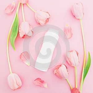 Shampoo and white tulips flowers on pink background. Flat lay, top view