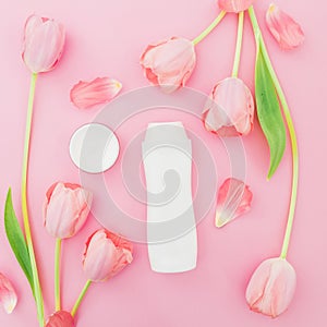 Shampoo and white tulips flowers on pink background. Flat lay, top view