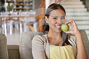 In shape and feeling great. Portrait of an attractive young woman eating an apple while relaxing on a sofa.