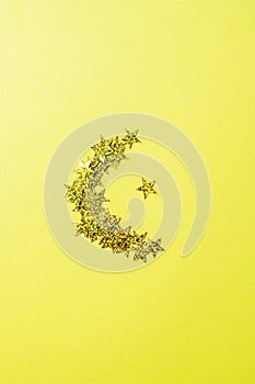 Shape of moon from glowing glitters. Yellow background and top view