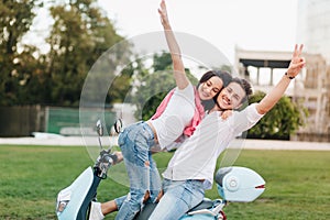 Shapely female model posing on scooter with happy smile near boyfriend in white shirt. Ecstatic young people enjoying