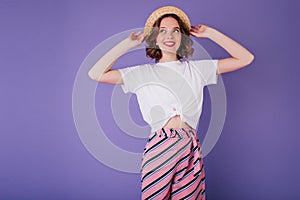 Shapely lady in white t-shirt and vintage hat posing in studio with smile. Indoor photo of glad eur