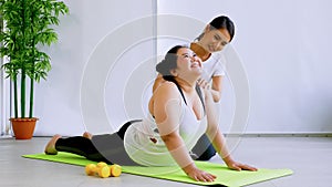 Shapely woman helping chubby woman doing exercise in finess room