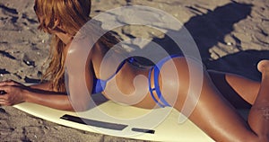 Shapely young woman sunbathing on a surfboard