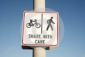 Share with care warning sign on a shared path for pedestrians and cyclists against a clear blue sky background