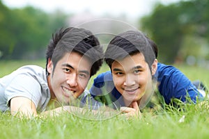 They share a love of the outdoors. Cute young gay Asian couple smiling together while lying on the grass.