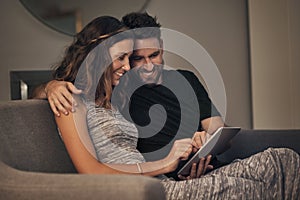 Share your interests, share the love. a young couple using a digital tablet together while relaxing on the sofa at home.