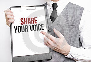 SHARE YOUR VOICE inscription on a notebook in the hands of a businessman on a gray background, a man points with a finger to the