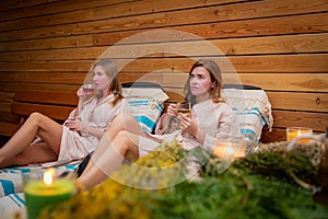 two women are sitting on a bed drinking wine