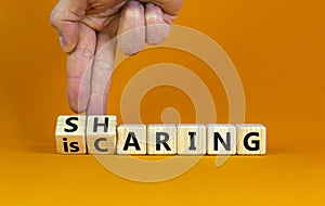 Sharing is caring symbol. Businessman turns wooden cubes with words `sharing is caring`. Beautiful orange table, orange backgrou