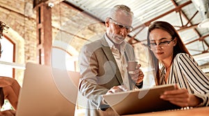 Sharing experience. Senior man in formal wear holding coffee cup and explaining something to his young female colleague