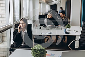 Sharing good business news. Attractive young woman talking on the mobile phone and smiling while sitting at her working place in