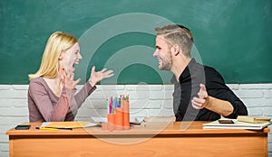 Sharing good news. Happy couple studying in classroom. Teacher and schoolmaster sitting at desk. Handsome man and pretty