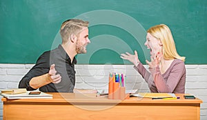 Sharing good news. Happy couple studying in classroom. Teacher and schoolmaster sitting at desk. Handsome man and pretty