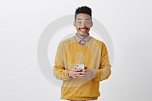 Sharing great news with friend. Portrait of happy thrilled dark-skinned man in trendy outfit, holding smartphone, gazing