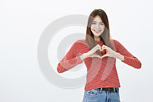 Sharing love and friendliness with friends. Attractive positive female student in casual outfit, showing heart gesture