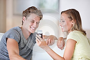 Sharing memories. A young couple looking at their cellphone in their living room.