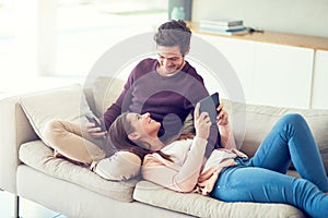 Sharing more than one connection. a smiling young couple using digital tablets while relaxing together on the sofa at