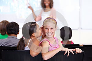 Sharing a secret. A young schoolgirl whispering into her friends ear during class.