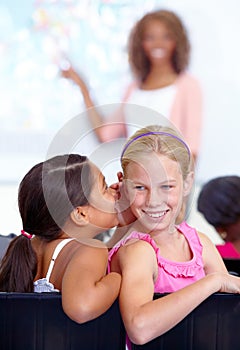 Sharing a secret. A young schoolgirl whispering into her friends ear during class.