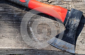 A sharp ax with an ergonomic rubberized handle on a wooden background. The ax is intended for rough, rough processing of wood. Has