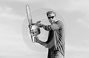 Sharp blade. Handsome man with chainsaw blue sky background. Gardener lumberjack equipment. Lumberjack with chainsaw in