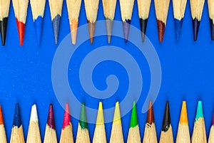 Sharp color pencils border, close-up to the sharp school pencils on a bright blue office table desktop background, top