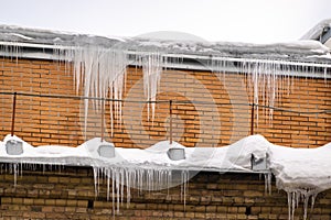 Sharp icicles hanging on the edge of the roof. Melting snow forms icicle