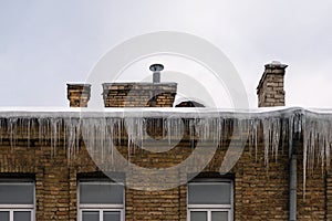 Sharp icicles hanging on the edge of the roof. Melting snow forms icicle