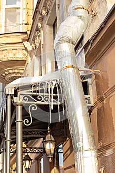 Sharp icicles a lot and melted snow hanging from eaves of roof and downpipe. Vertical photo