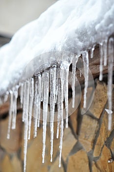 Sharp icicles and melted snow hanging from eaves of roof. Beautiful transparent icicles