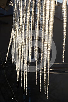 Sharp icicles and melted snow hanging from eaves of roof. Beautiful transparent icicles slowly gliding of a roof