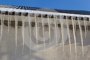 Sharp icicles and melted snow hanging from eaves of roof. Beautiful transparent icicles slowly gliding of a roof