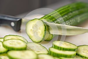 A sharp kitchen knife cuts through a cucumber on a board.