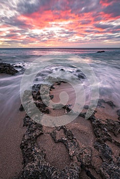 Sharp pink sunset over water movements on beach rocks in Kenting, Taiwan