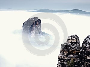 Sharp sandstone rock empire sticking out from heavy fog. Deep misty valley