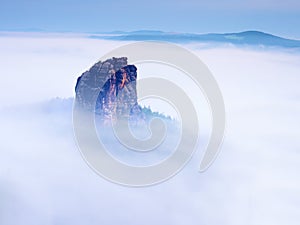 Sharp sandstone rock empire sticking out from heavy fog. Deep misty valley