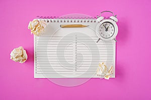 Sharpen pencil and white alarm clock on planner and crumpled paper balls on pink paper