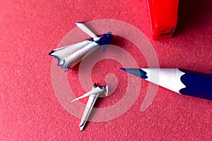 Sharpened blue pencil with sharpener on a red background