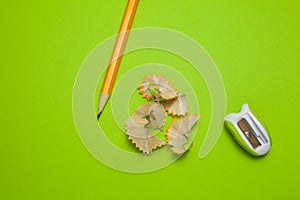 Sharpened pencil and sharpener on green background, top view