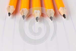 Sharpened pencils lying on a notebook sheet in a strip
