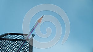 A sharpened simple pencil stands in a mesh jar on a blue background. Sharpened pencil tip.