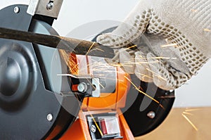 Sharpening the blade of a lawn mower with an electric sharpener. Hands in work gloves hold and sharpen the blade