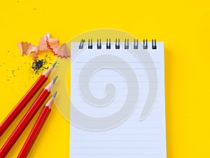 Sharpening a red pencil sharpener and the note book On yellow background.