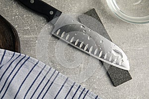 Sharpening stone, knife and water on grey table, flat lay