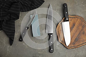 Sharpening stone and knives on grey table, flat lay